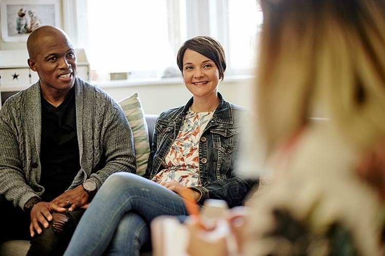 Counseling, therapy and happy couple talking to a therapist on modern office sofa at clinic. Psychology communication, discussion and interracial man and woman speaking to relationship psychologist.
