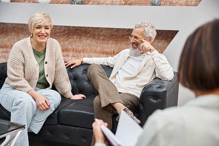 Smiling middle aged couple sitting on leather couch and looking at psychologist during consultation