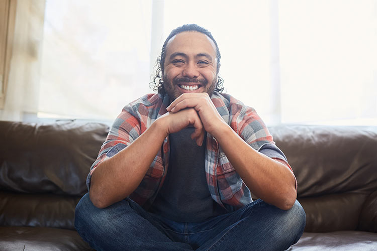 Resilient and smiling young latino man sitting on therapy couch